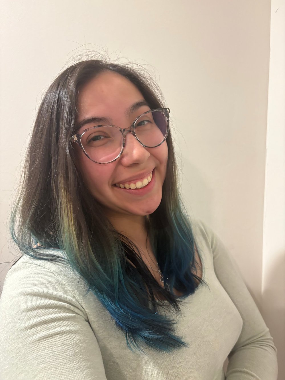 Julia Perez smiling, wearing glasses and a sage green top, with long dark hair that fades to blue at the ends.