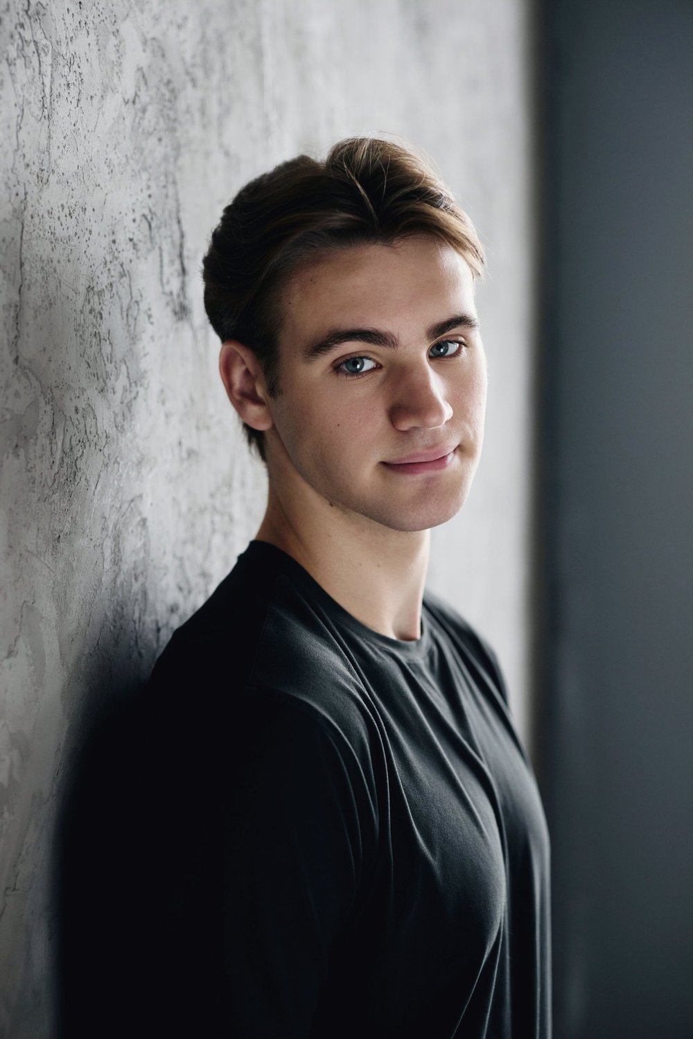 Will Williams leaning against a textured gray wall in a dark T-shirt, looking toward the camera.